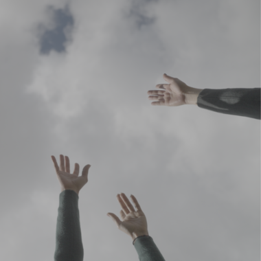 Drei nach oben gestreckte Hände vor einem wolkigen Himmel. Die Hände gehören unterschiedlichen Personen, die außerhalb des Bildrandes stehen.