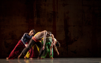 Eine Szene aus 2x4 von A.I.M by Kyle Abraham. Eine Tänzerin mit grüner Hose und weißem Shirt steht in einer großen tänzerischen Pose auf der Bühne. Sie macht einen Ausfallschritt, hat die Arme zu den Seiten ausgebreitet und lehnt sich mit dem Oberkörper nach vorne. Auf dem Bild steht in Ticket-Special, A.I.M by Kyle Abraham, Mixed Bill