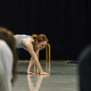 Ein Foto aus einem Workshop von Cara Rother. Es zeigt Cara Rother, die mit beiden Händen den Boden berührt und dabei lächelt.