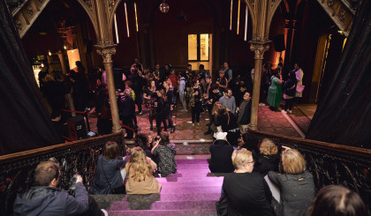 The photo shows a party situation in the Cumberlandsche Bar. The photo was taken from the stairs down into the bar area and shows various people sitting on the steps or dancing in the bar area. The light is dimmed and a disco ball is spinning on the ceiling.