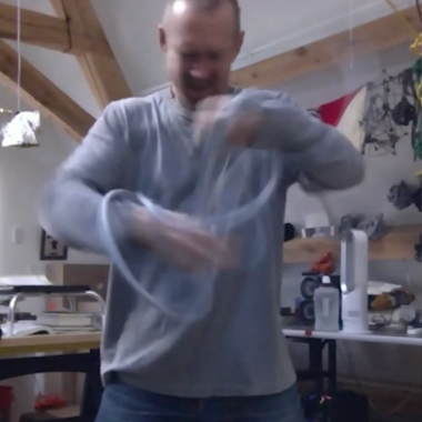 Ein Videostill der Arbeit TRI TEMPI (2023) von William Forsythe. Es ist ein Tryptichon und zeigt Forsythe stehend mit einem Objekt in der Hand.