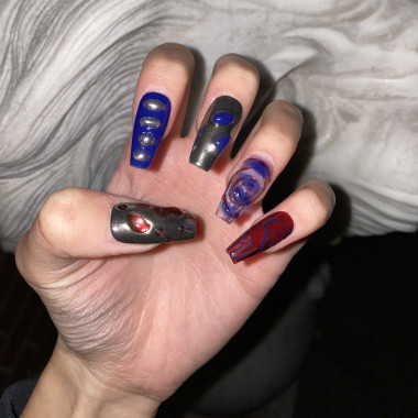 Eine manikürte Hand. Die Fingernägel sind lang und weisen jeweils unterschiedliche Nageldesigns auf. Einige Nägel sind blau, andere rötlich, darauf verschiedene organische Formen.
