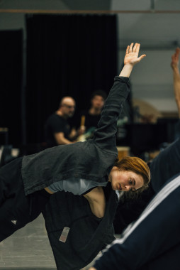 Eine Szene aus einem Workshop von Cara Rother. Es zeigt Cara Rother bei einer Art Dehnübung. Cara ist sportlich gekleidet und streckt die linke Hand in die Luft. 