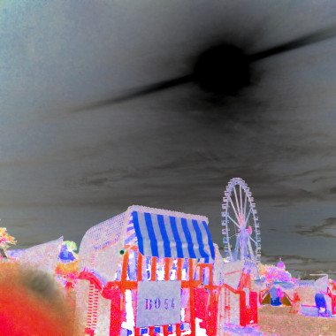 Ein in blau und rot Tönen gefärbte Negativaufnahme eines Jahrmarkt- oder Strandbereichs mit Strandkörben im Vordergrund und einem großen Riesenrad im Hintergrund unter einem dunklen Himmel.